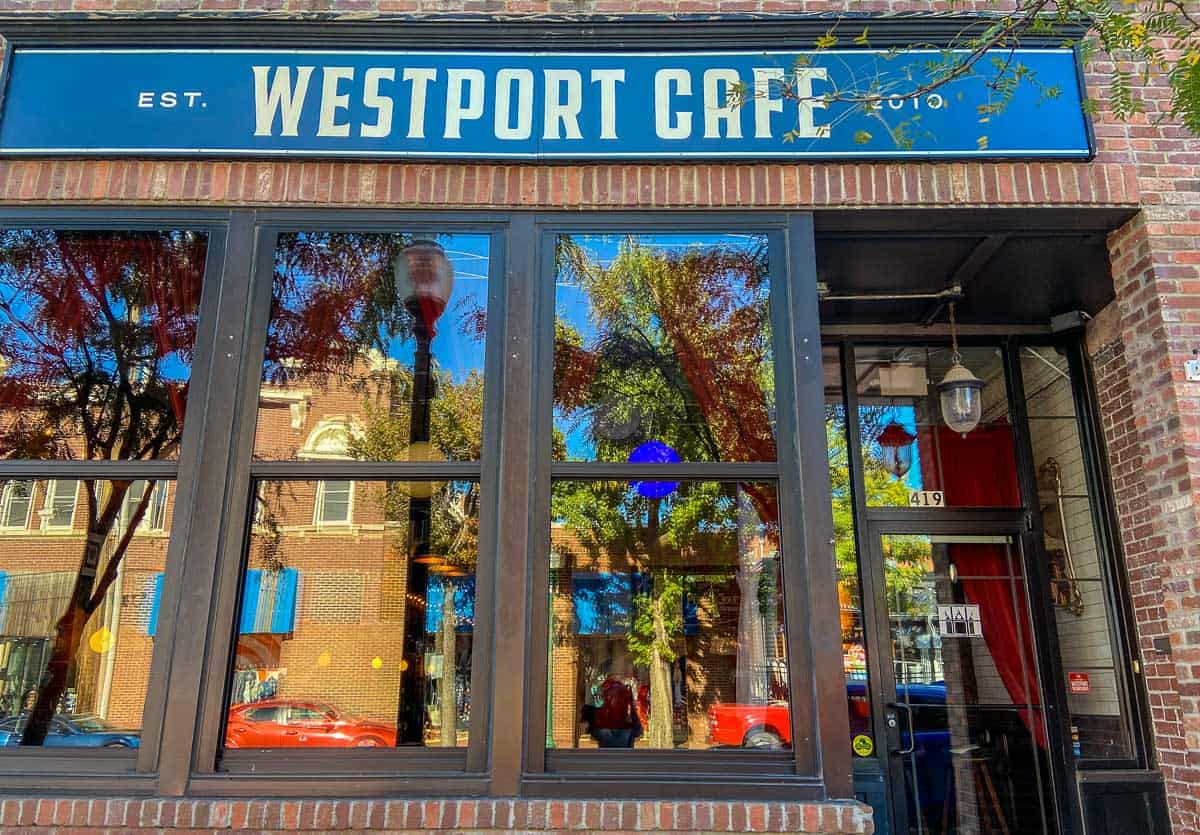 The exterior of Westport Cafe on a sunny day. The cars and buildings in front of it are reflecting off the window.
