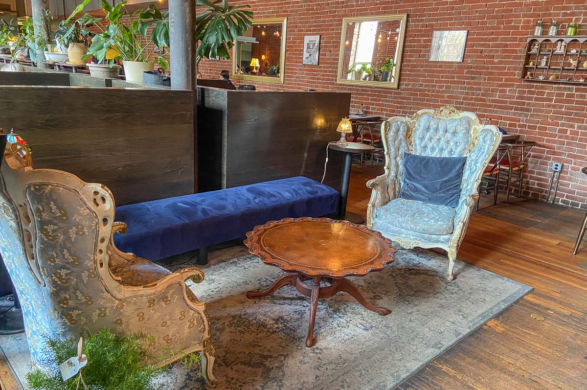 The front lobby of the charming restaurant, Lula Southern Cookhouse. There are two antique chairs and a blue velvet bench.