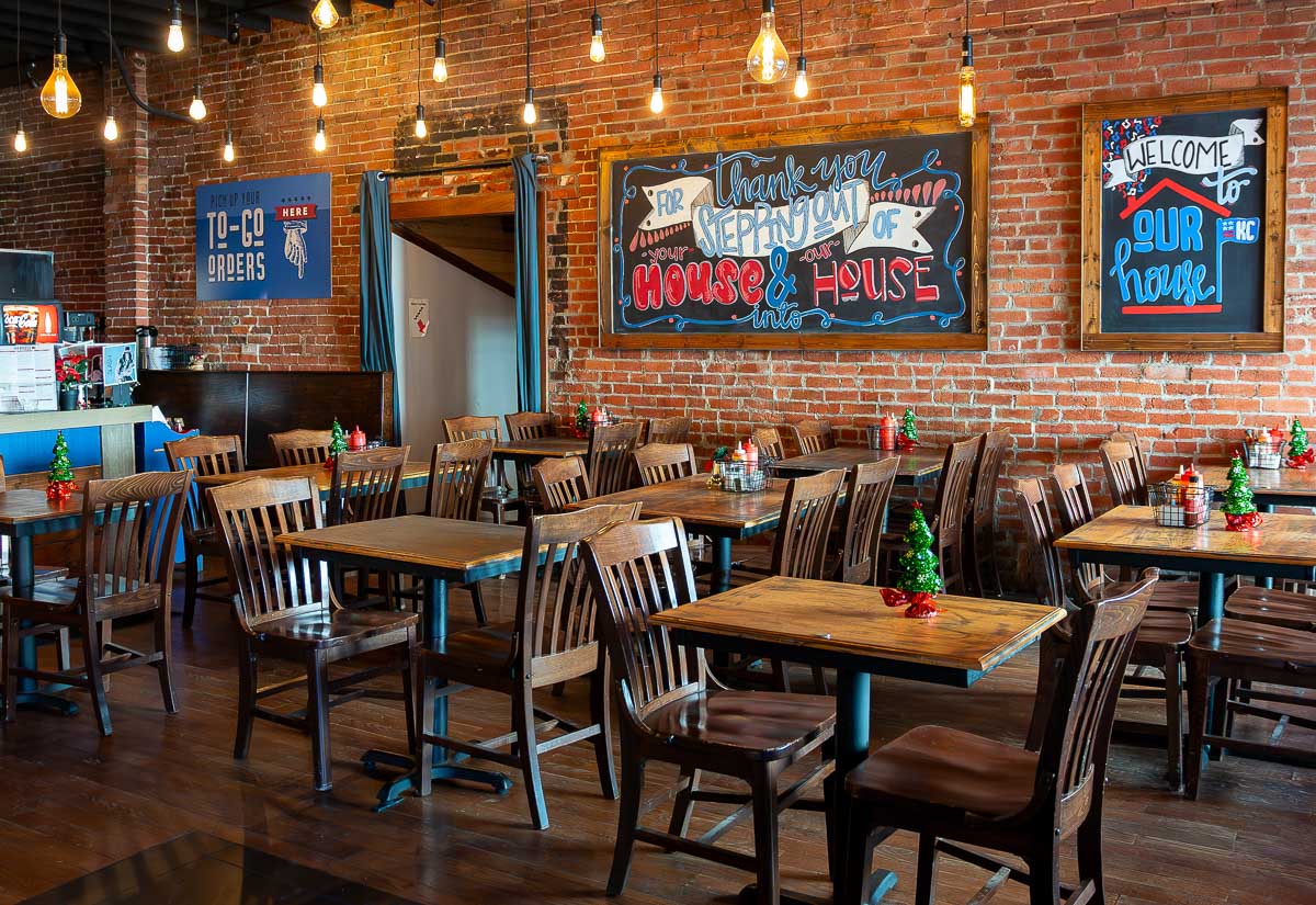 The main dining area at OurHouseKC with brown chairs and tables. It's also Christmastime so there are mini trees on each table.