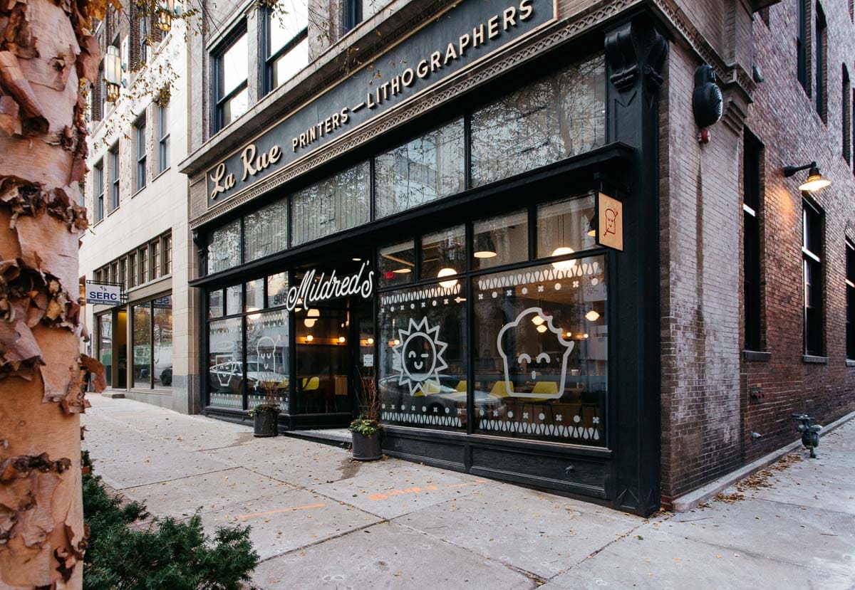 The exterior of a restaurant spot located in downtown KC, Mildred's. It has white painted shapes on the front - including a muffin, sun, toast, and coffee.