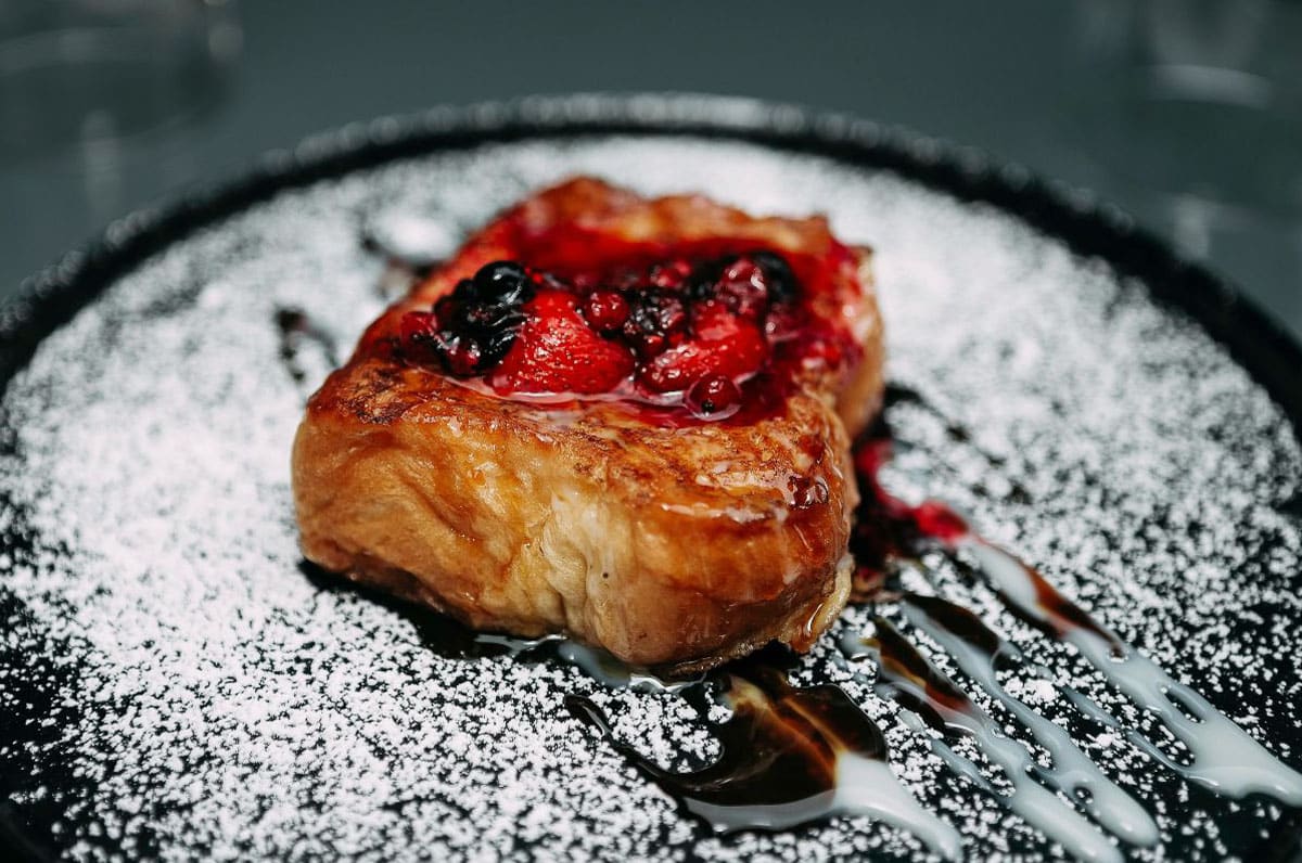 Brioche french toast with berries and powdered sugar sprinkled on top.
